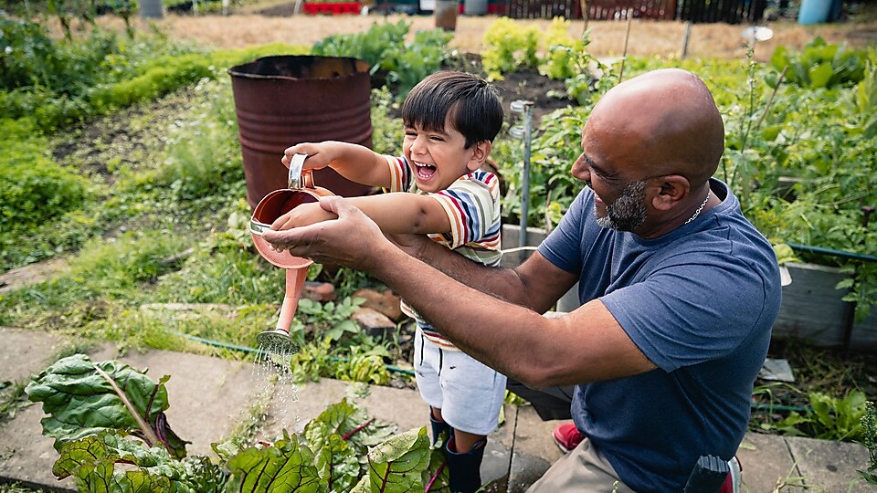 Un homme aide un enfant souriant à arroser des plantes dans un jardin