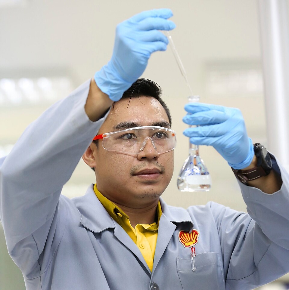 Een wetenschapper van Shell met een veiligheidsbril druppelt vloeistof uit een pipet in een beker