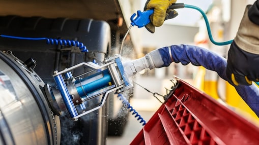 Gros plan sur une opération de ravitaillement en GNL : une main gantée actionne la poignée bleue d’un tuyau de remplissage. De la vapeur froide s’échappe autour du tuyau isolé et de l’accouplement métallique relié au réservoir d’un véhicule lourd.