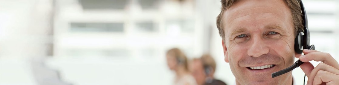 A man wearing a headset and having a phone call. Two more people in the background doing the same - blurred out.