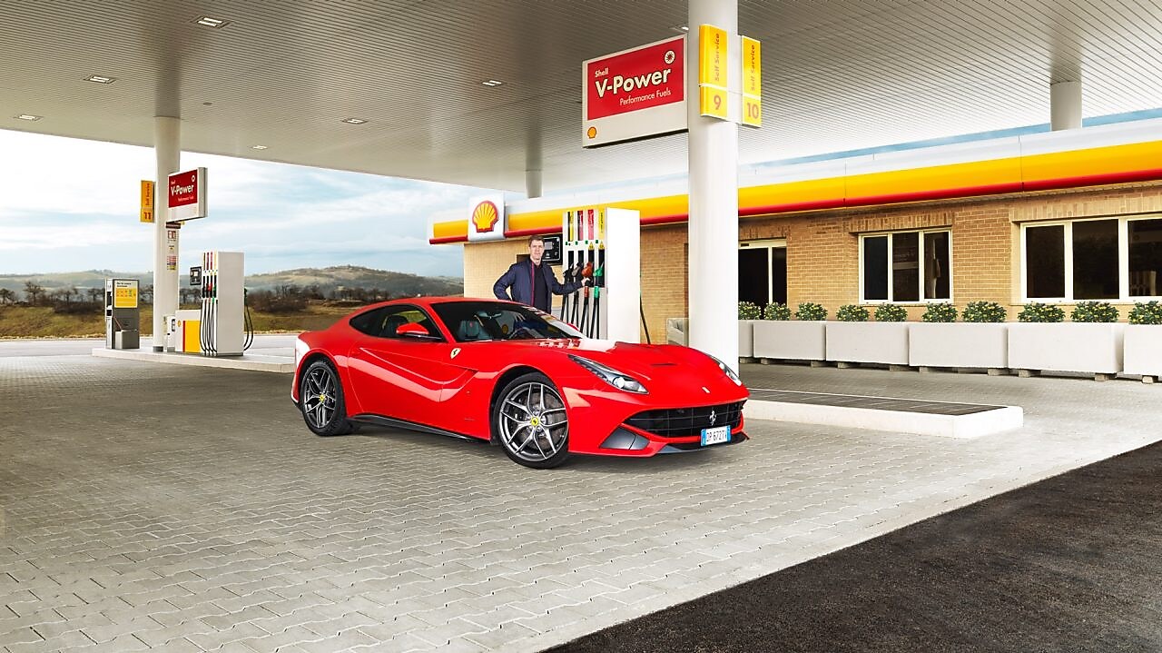 Une Ferrari rouge arrêtée à la pompe d'une station Shell avec un homme qui s'apprête à faire le plein