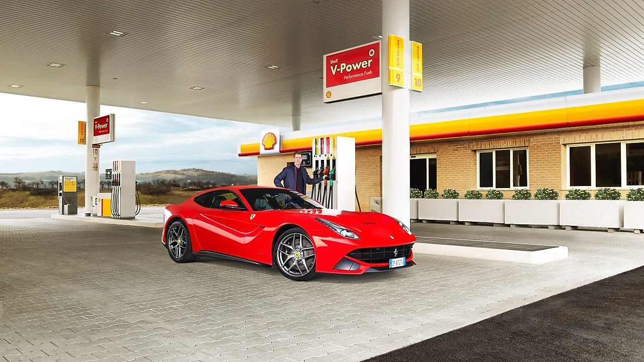 Une Ferrari rouge arrêtée à la pompe d'une station Shell avec un homme qui s'apprête à faire le plein