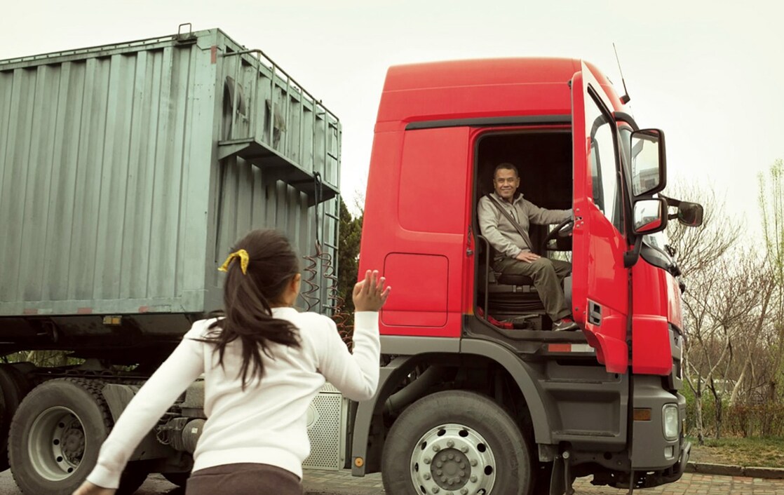 Homme à bord d’un camion rouge faisant un petit coucou à sa fille au travers de la portière ouverte