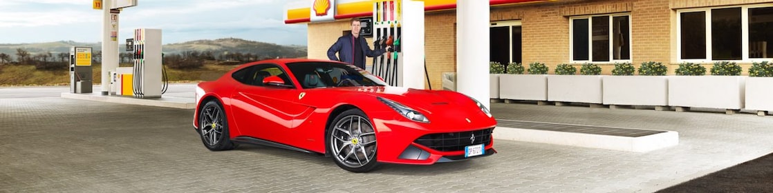 Une Ferrari rouge arrêtée à la pompe d'une station Shell avec un homme qui s'apprête à faire le plein