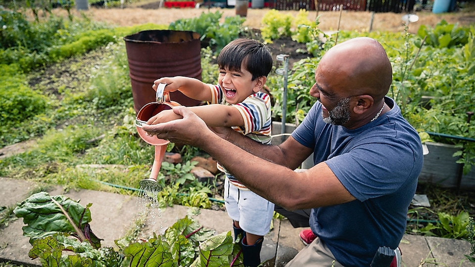 Man helpt lachend kind planten in de tuin water te geven