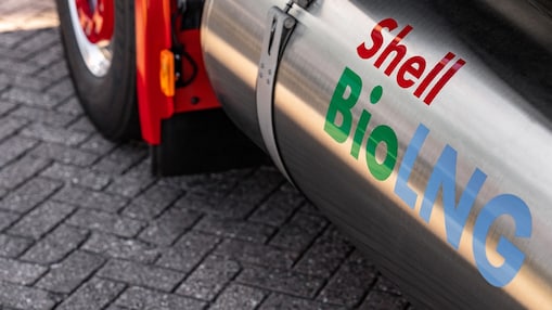 Close‑up van een metalen tank van een zwaar voertuig met het opschrift “Shell BioLNG” in gekleurde letters. Een deel van het voertuig en het wegdek van klinkers zijn zichtbaar op de achtergrond.