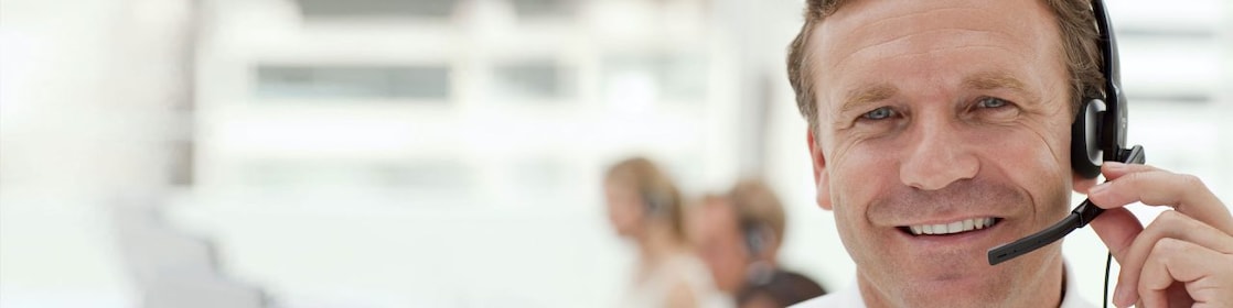 A man wearing a headset and having a phone call. Two more people in the background doing the same - blurred out.