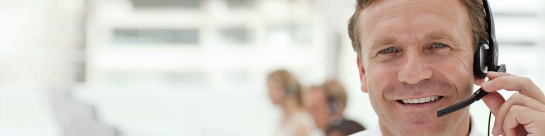 A man wearing a headset and having a phone call. Two more people in the background doing the same - blurred out.