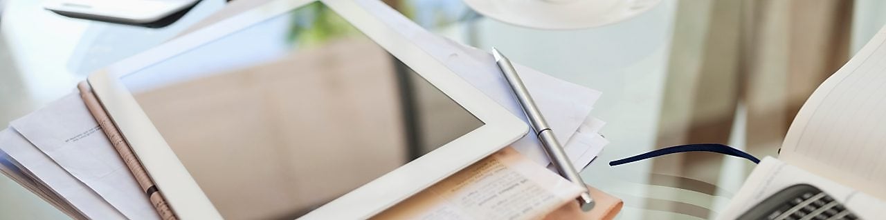 Tablet computer, newspaper, coffee cup and cell phone on desk
