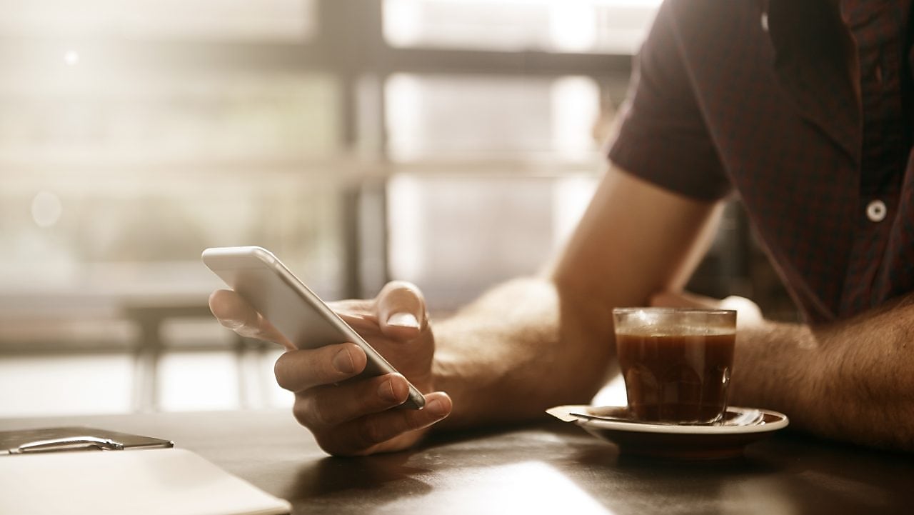 Een man met een mobiel en een tas koffie