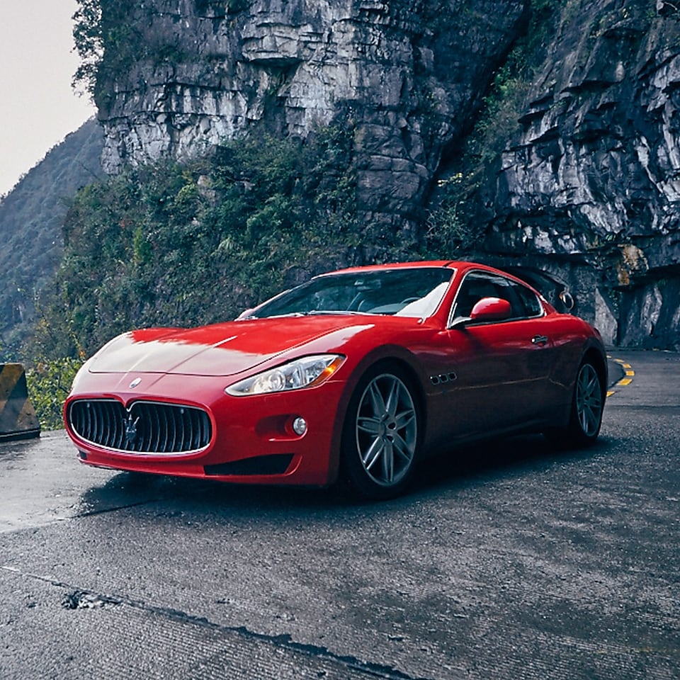 Een rode Maserati met standaard Shell Helix Ultra-product staat trots op een prachtige bergweg